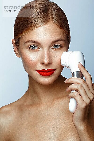 Schönes Mädchen mit roten Lippen und klassischem Make-up mit Massagepinsel in der Hand. Schönes Gesicht. Foto im Studio aufgenommen