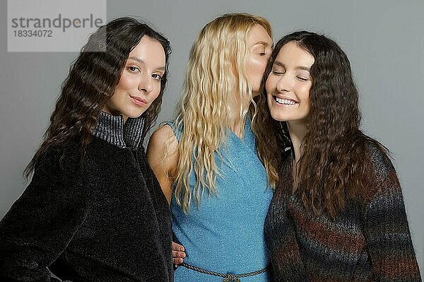 Drei attraktive Mädchen in Wollmänteln posieren im Studio. Klatschmädchen
