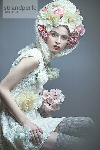 Schönes Mädchen mit einem Kopftuch im russischen Stil  mit großen Blumen auf dem Kopf und roten Lippen. Schönheit Gesicht. Bild im Studio auf einem grauen Hintergrund genommen