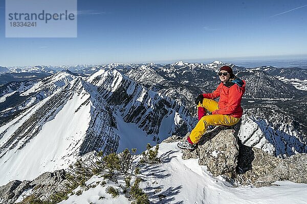 Skitourengeherin sitz auf einem Felsen  am Gipfel des Sonntagshorn  hinten verschneite Gipfel des Hirscheck und Vorderlahnerkopf  Bergpanorama  Chiemgauer Alpen  Bayern  Deutschland  Europa