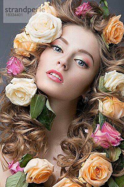 Schönes Mädchen mit vielen Blumen im Haar und leuchtend rosa Make-up. Frühling Bild. Schönheit Gesicht. Bild im Studio auf einem grauen Hintergrund aufgenommen