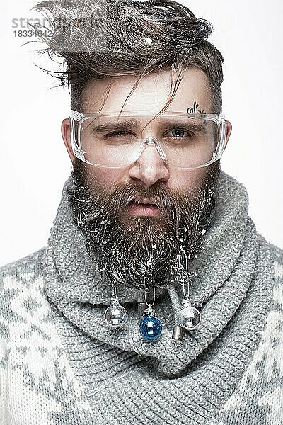 Lustiger bärtiger Mann in einem Neujahrsbild mit Schnee und Dekorationen auf seinem Bart. Fest der Weihnacht. Fotos im Studio aufgenommen