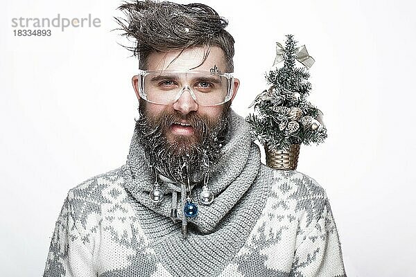 Lustiger bärtiger Mann in einem Neujahrsbild mit Schnee und Dekorationen auf seinem Bart. Fest der Weihnacht. Fotos im Studio aufgenommen