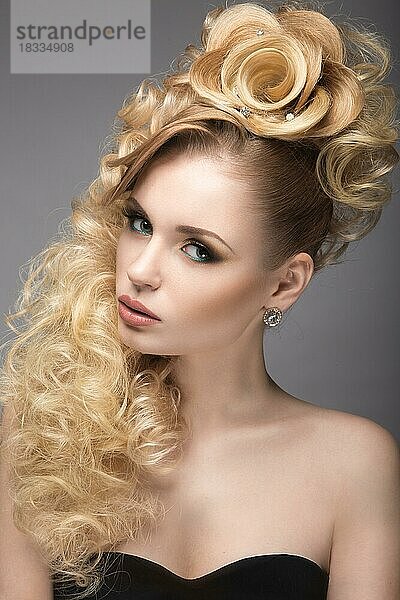 Schönes blondes Mädchen im Abendkleid mit einer ungewöhnlichen Frisur in Form von Rosen und hellem Make-up. Schönheit Gesicht. Bild im Studio auf einem grauen Hintergrund genommen