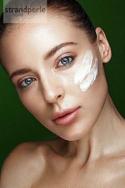 Schönes frisches Mädchen mit Kosmetikcreme auf dem Gesicht  natürliches Make-up und grüne Blätter. Schönes Gesicht. Foto im Studio aufgenommen