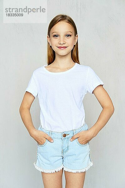Junges sportliches Mädchen in weißem T-Shirt mit Händen in Jeans-Shorts posiert im Studio