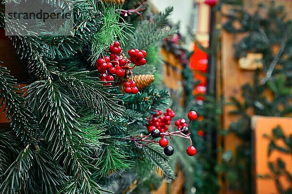 Nahaufnahme einer saisonalen Winterdekoration aus künstlichen roten Beeren und Tannenzweigen an einem traditionellen Verkaufsstand auf dem Weihnachtsmarkt