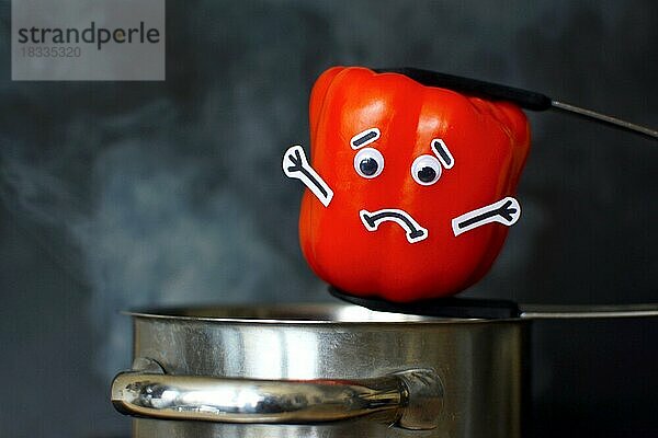 Rote Paprikaschote mit traurigem Gesicht und Glotzaugen  die in einen dampfenden Kochtopf auf dunklem schwarzem Hintergrund gelegt wird  Konzept für Gemüse  das beim Kochen Vitamine verliert