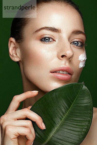 Schönes frisches Mädchen mit Kosmetikcreme auf dem Gesicht  natürliches Make-up und grüne Blätter. Schönes Gesicht. Foto im Studio aufgenommen