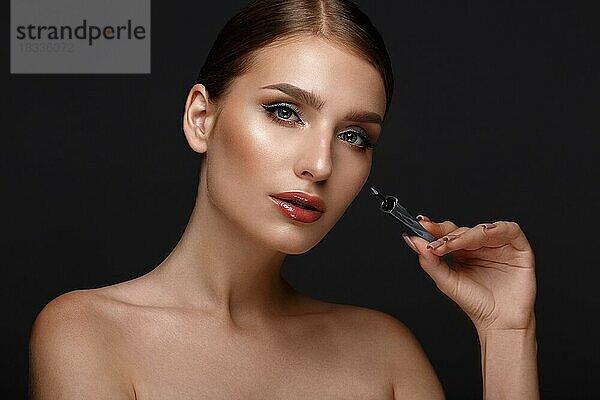 Schönes Mädchen mit sexy Lippen und klassischen Make-up mit kosmetischen blauen Eyeliner in der Hand. Schönes Gesicht. Foto im Studio aufgenommen