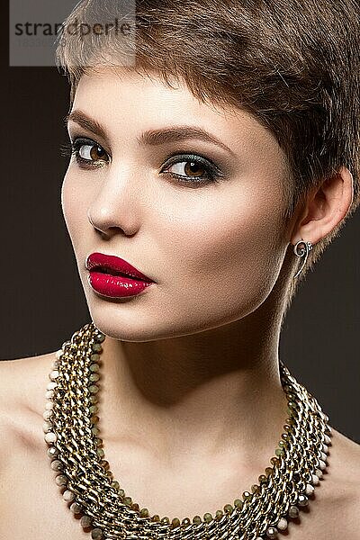 Schöne brünette Frau mit perfekter Haut  hellem Make-up und Goldschmuck. Schönes Gesicht. Bild im Studio auf einem grauen Hintergrund genommen