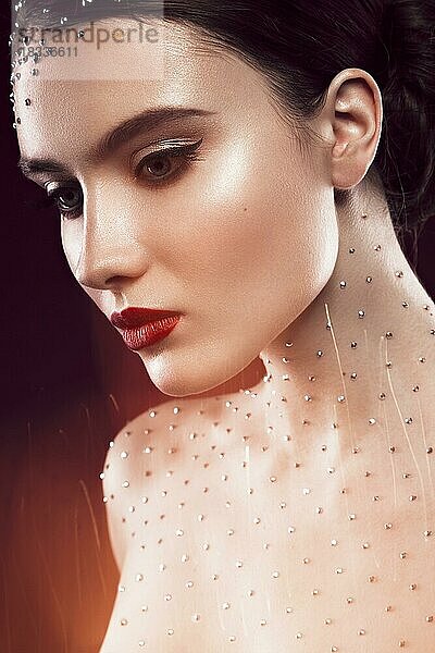 Porträt eines schönen Mädchens mit einem hellen Make-up  roten Lippen und Kristallen auf dem Körper. Die Schönheit des Gesichts. Fotos im Studio geschossen