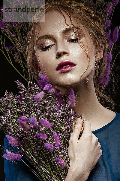 Schönes Mädchen mit einem sanften Make-up und Frisur in Form von Zöpfen  trockene Blumen in ihren Händen. Schönes Gesicht. Bild im Studio aufgenommen