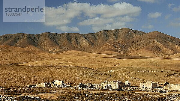 Inselinneres  karge Landschaft  rotbraune Hügel  Gebäuderuinen nah  blauer Himmel  weiße Wolken  Fuerteventura  Kanarische Inseln  Spanien  Europa