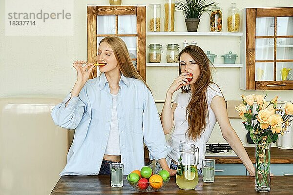 Zwei schöne junge Frauen essen Früchte in der Küche