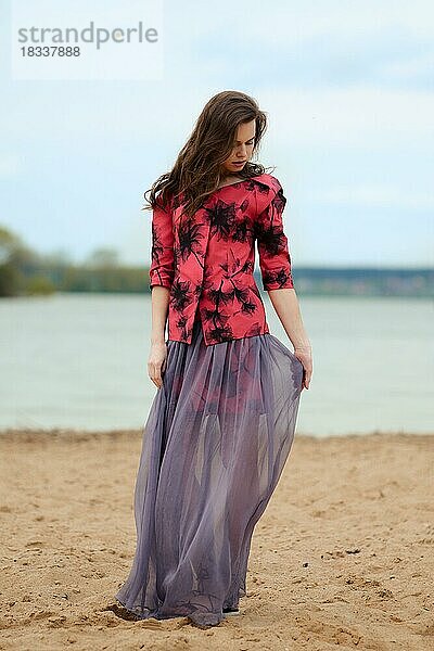 Romantisches Lifestyle-Porträt einer jungen Frau in transparentem Rock und Jacke am Strand