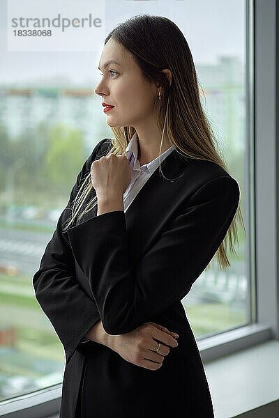 Porträt einer modernen Geschäftsfrau  die durch ein Bürofenster schaut