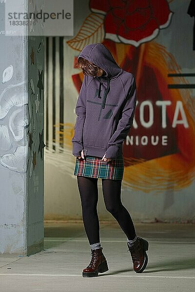 Tricky Girl posiert in violettem Fleece-Sweatshirt mit Kapuze. Gesicht verbergen
