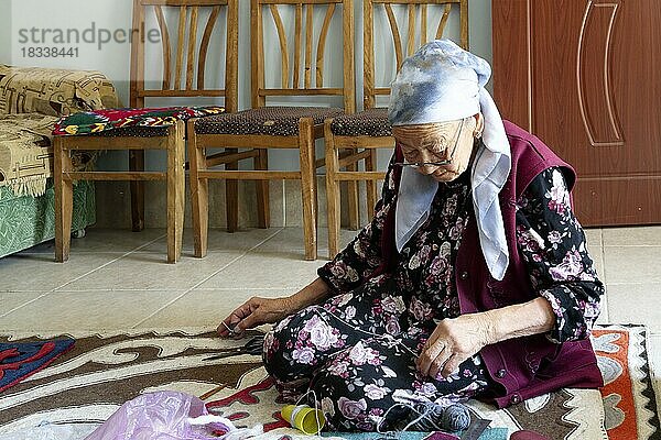 Alte Frau sitzt auf dem Boden und näht Teppiche in einer handwerklichen Fabrik  Kochkor  Kirgisistan