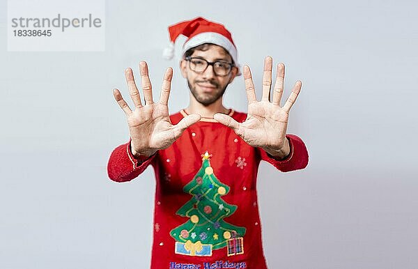 Mann mit Weihnachtsmütze  der mit den Fingern die Zahl zehn zählt. Weihnachten junger Mann zählt die Zahl zehn mit den Händen. Konzept der Mann im Weihnachtskostüm Zählen der Zahl zehn isoliert