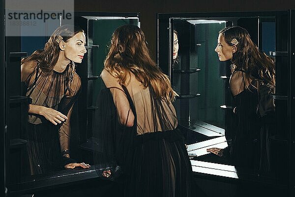 Low-Key-Foto von attraktiven Mädchen schaut in den Spiegel in transparenten Kleid