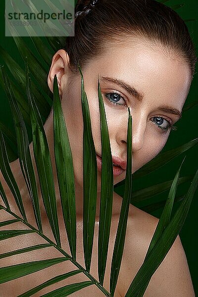 Schönes frisches Mädchen mit Kosmetikcreme auf dem Gesicht  natürliches Make-up und grüne Blätter. Schönes Gesicht. Foto im Studio aufgenommen