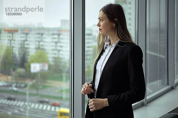 Hübsche Angestellte eines Bauunternehmens  die durch das Fenster ihres Büros auf der Baustelle schaut