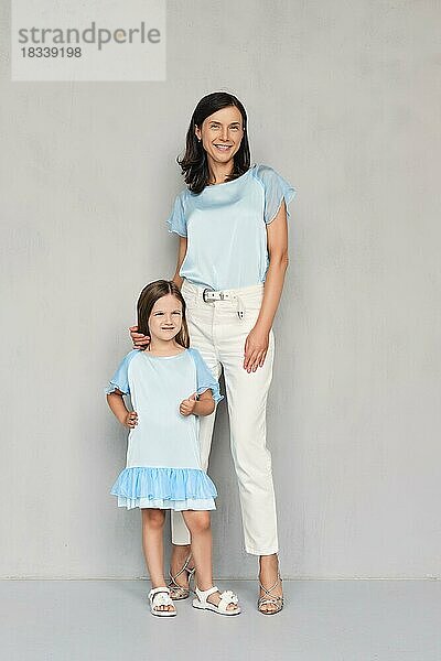 Stilvoll und trendy Mutter und ihre junge Tochter posieren zusammen in der Nähe von grauen Wand