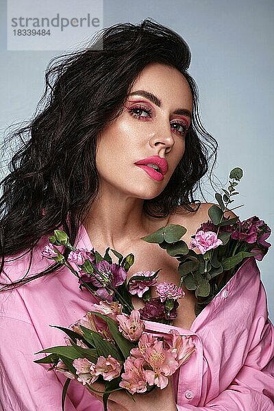 Schöne brünette Mädchen mit einem sanften rosa romantischen Make-up  rosa Lippen  hält Blumen. Die Schönheit des Gesichts. Porträtaufnahme im Studio