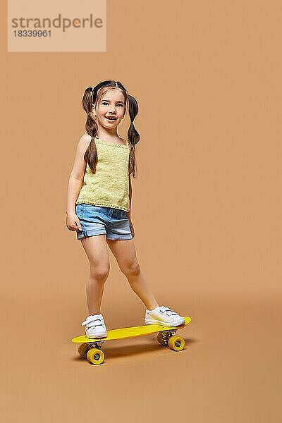 Junges glückliches Mädchen lernt auf dem Skateboard zu fahren