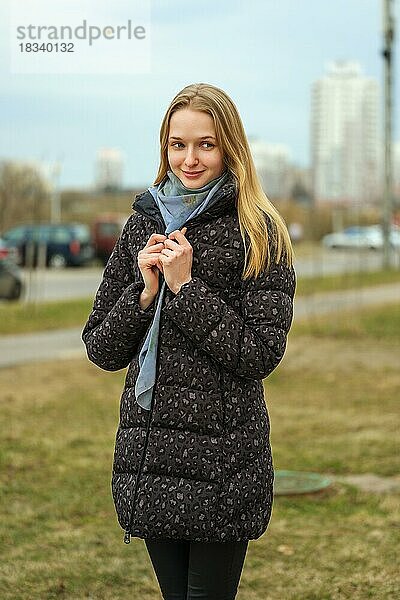 Fröhliches Mädchen in Jeans und Daunenjacke geht die Straße in einem Wohngebiet mit hohen Häusern entlang