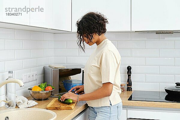Junge afrikanisch-amerikanische Hausfrau schneidet in der Küche Gurke für Salat