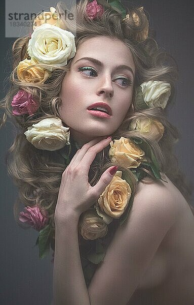 Schönes Mädchen mit vielen Blumen im Haar und leuchtend rosa Make-up. Frühling Bild. Schönheit Gesicht. Bild im Studio auf einem grauen Hintergrund aufgenommen