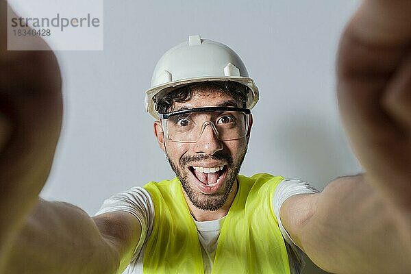 Lächelnder männlicher Ingenieur  der ein Selfie macht und in die Kamera schaut. Funny builder engineer taking a selfie isolated  Engineer taking a selfie isolated. Blick auf männliche Ingenieur  der ein Selfie isoliert
