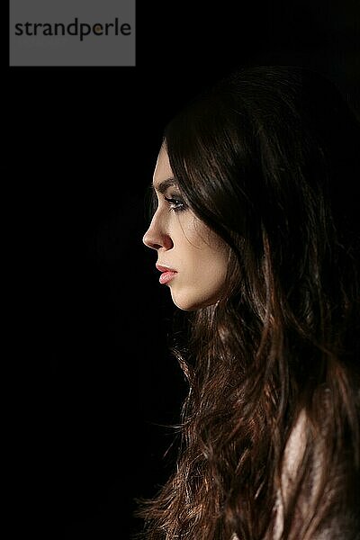Porträt im Profil eines schönen Mädchens mit langen lockigen Haaren  das gerade in die Dunkelheit blickt