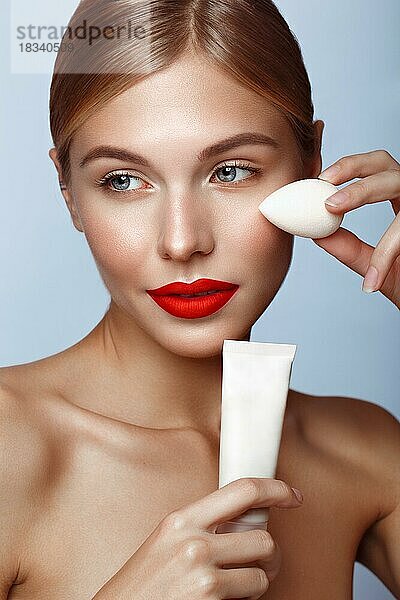 Schönes Mädchen mit roten Lippen und klassischen Make-up mit Stiftung und Schwamm in der Hand. Schönes Gesicht. Foto im Studio aufgenommen