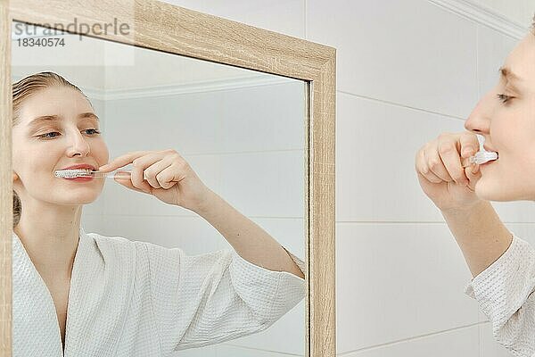 Junge Frau putzt ihre Zähne vor dem Spiegel im Badezimmer am Morgen