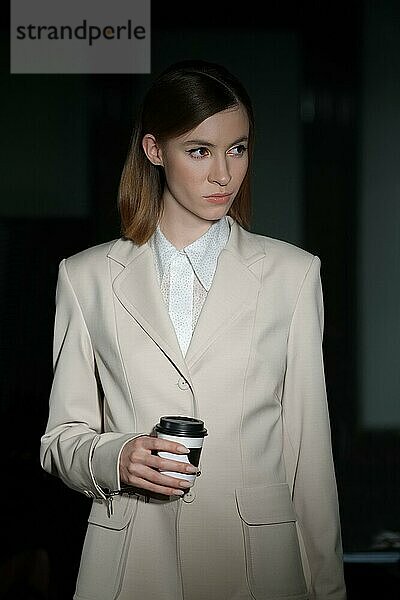 Seriöses Mädchen im Business-Anzug mit Kaffeebecher zum Mitnehmen in der Hand