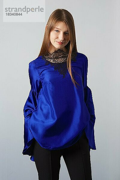 Attraktive Mode-Modell in blauer Seide Bluse mit Schmetterling Ärmel posiert für Lookbook in der Nähe von grauen Wand