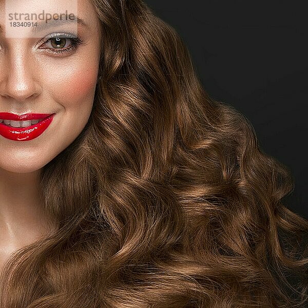 Schönes braunhaariges Mädchen mit perfekt gelocktem Haar  roten Lippen und klassischem Make-up. Schönheit Gesicht und Haar. Bild im Studio aufgenommen