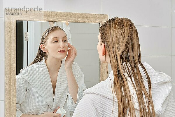 Junge Frau  die ihr Gesicht nach dem Duschen mit einer Creme eincremt