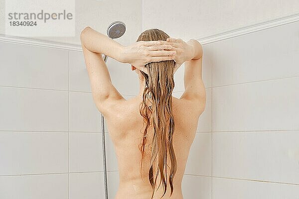 Rückenansicht einer jungen Frau mit gesunder Haut wäscht ihr Haar mit Shampoo im Badezimmer