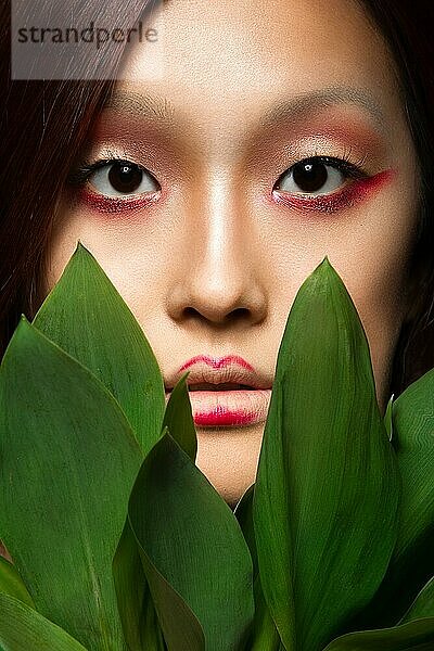 Schönes asiatisches Mädchen mit einem hellen Make-up Kunst in grünen Blättern. Schönes Gesicht. Kreatives Bild. Bild im Studio aufgenommen