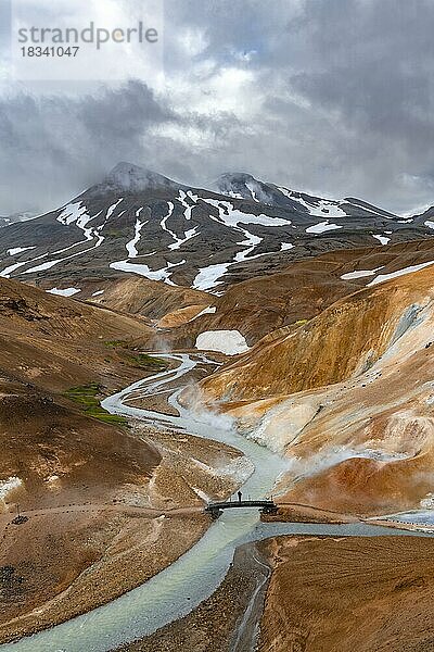 Tourist auf Brücke über dampfenden Bach zwischen bunten Rhyolith Bergen mit Schneefeldern  Geothermalgebiet Hveradalir  Kerlingarfjöll  isländisches Hochland  Island  Europa