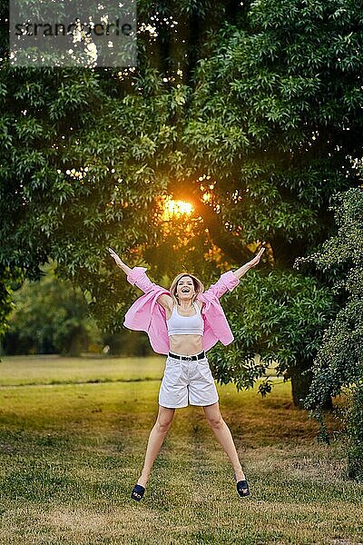 Glückliche junge Frau springt bei Sonnenuntergang im Park