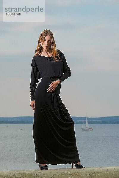 Attraktive Mode-Modell in langen schwarzen Kleid posiert auf dem Pier
