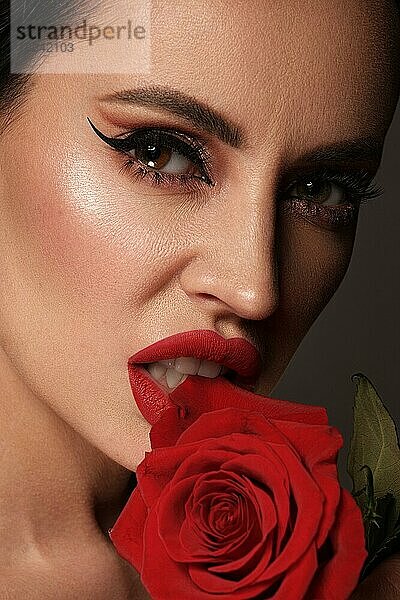 Schöne brünette Frau mit klassischem Make-up  roten Lippen und Blumen in der Hand. Die Schönheit des Gesichts. Porträtaufnahme im Studio