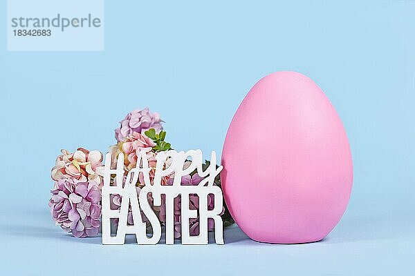 Großes rosa Osterei  Hortensienblüten und Text Frohe Ostern auf blauem Hintergrund