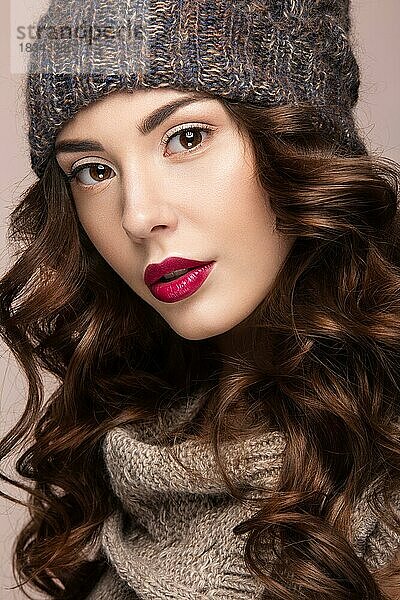 Schönes Mädchen mit sanftem Make-up  Locken in brauner Winterstrickmütze. Warmes Winterbild. Schönes Gesicht. Bild im Studio aufgenommen