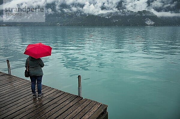 Ältere Frau  Best-Ager  mit rotem Regenschirm  schlechtes Wetter  Seepromenade am Brienzersee  Brienz  Kanton Bern  Berner Oberland  Schweiz  Europa